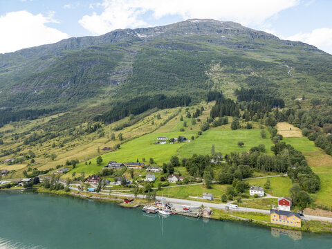 Aerial view of the vibrant turquoise waters meet the lush green fields and the towering mountain, creating a striking contrast of color and texture, Olden, Vestland, Norway.