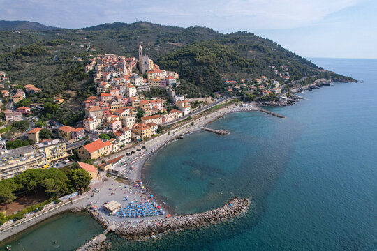 Aerial view of the medieval village cascading down the hillside towards the azure sea, the beach bustling with life under the warm Italian sun, Cervo, Liguria, Italy.