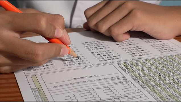 Close-up of student hand using pencil to fill multiple choice answers on standardized exam sheet, educational test concept.