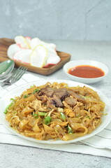 Char Kway Teow, fried rice flat noodles with beef, egg, and vegetables on a white plate, Indonesian dish.