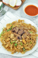 Char Kway Teow, fried rice flat noodles with beef, egg, and vegetables on a white plate, Indonesian...