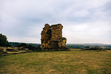 Weathered remains of an ancient stone structure in a vast open field under a cloudy sky
