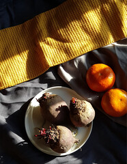 Still life arrangement of beets and oranges with a yellow textile.