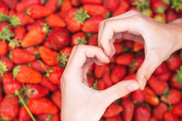 Hands making heart shape over fresh strawberries