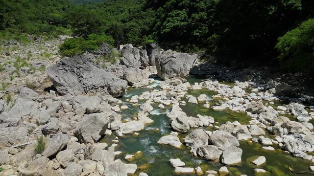 A low aerial shot tilts and moves sideways, revealing Tinipak River&rsquo;s winding white rocks and lush greenery, capturing the natural beauty from a close, dynamic perspective