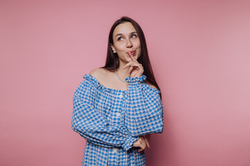 portrait of young woman thoughtfully poses with a finger on her lips on pink background