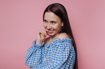 portrait of young woman bites her finger playfully while deep in thought, wearing a blue checkered...