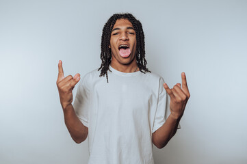 portrait of young man displays a rock gesture with his hands and sticks his tongue out, embodying...