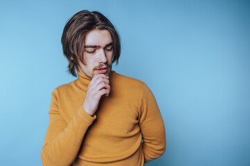 portrait of young man in a turtleneck poses thoughtfully, appearing contemplative on blue background