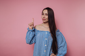 portrait of young woman is smiling and pointing up playfully, embodying joy and positivity on pink...