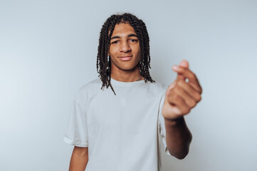 portrait of young man looks playfully at the camera while forming a heart shape with his fingers, radiating warmth and affection on light background
