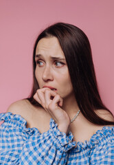 portrait of young nervous woman bites her nail, showcasing vulnerability and anxiety on pink...