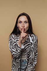portrait of young woman poses with a finger to her lips, asking for silence on calm yellow...