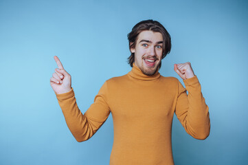 portrait of young man in a turtleneck excitedly points upward, conveying a sense of victory or...