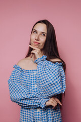 portrait of young woman poses with a finger on her chin on pink background