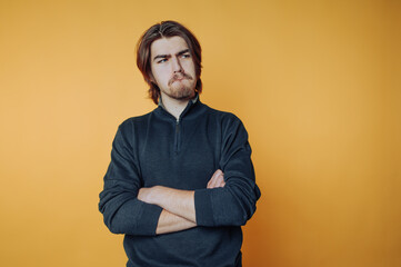 portrait of young man with a furrowed brow and crossed arms stands, conveying introspection on...
