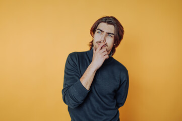 portrait of young man is in a pensive pose, looking up thoughtfully on yellow background