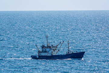 Fishing boat in blue sea and clear sky with birds flying overhead.