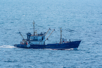 Fishing boat in blue sea and clear sky with birds flying overhead.