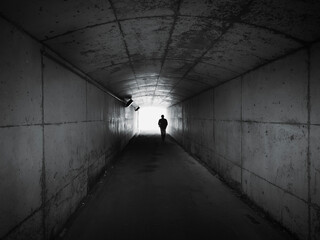 Silhouette people walking towards a Light at End of  Concrete tunnel perspective view