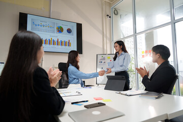 Businesswomen shaking hands while colleagues are clapping in the office meeting room