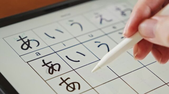 Close-up of a digital tablet displaying Japanese hiragana characters with a stylus writing practice strokes. Ideal for concepts of language learning, online education, and digital study. 4k video.
