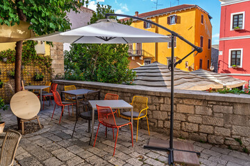 An empty street cafe with modern furniture set on a stone patio against colorful old buildings.Picturesque restaurant patio with tables, chairs, and umbrellas in a historic square in a European city