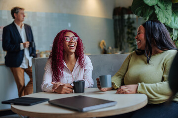 Coworkers laughing and talking during coffee break in office cafeteria