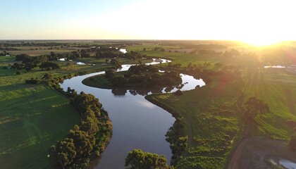 Aerial view of a serene river meandering through green pastures at golden hour