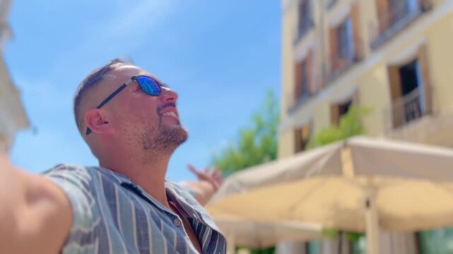 POV Point of view of male latin tourist enjoying vibrant Madrid cityscape, stretching arms wide under bright blue sky, embodying carefree travel spirit and summer freedom in Spanish urban landscape.