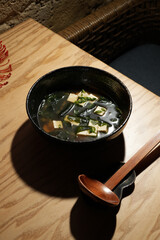 Gourmet miso soup with tofu and seaweed, served in a dark bowl with a wooden ladle