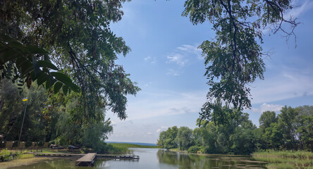 Summer river landscape with green trees, reflections and blue sky. Tourism