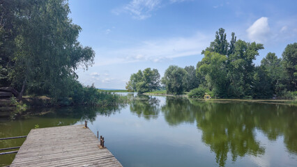 Summer river landscape with green trees, reflections and blue sky. Tourism