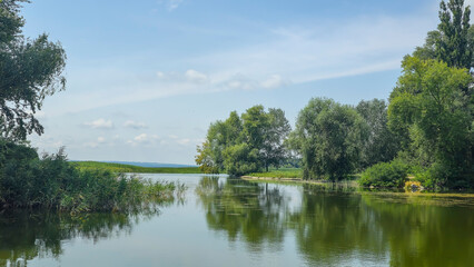 Summer river landscape with green trees, reflections and blue sky. Tourism
