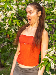 Young woman sneezes in the park against the background of a flowering tree. Allergy to pollen...