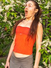 Young woman sneezes in the park against the background of a flowering tree. Allergy to pollen concept.