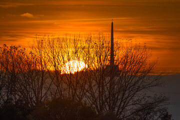 Red orange sunset with sun disk behind TV tower and trees