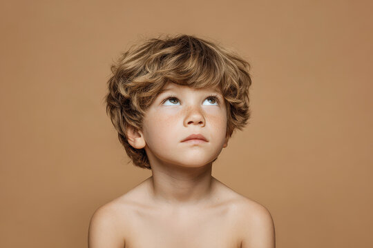 young boy gazes upwards with despair in his eyes against clean solid color background