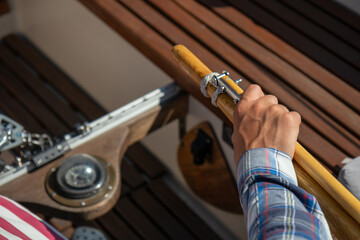 Skilled young man steering a sailboat with wooden tiller on the open waters of the Gulf of Finland. Good sailing experience, maritime adventure, summer leisure, connection to the sea