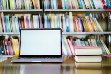 There is a laptop with a white screen and a book placed on the table in the library.
