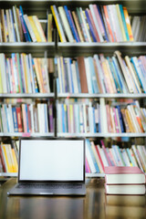 There is a laptop with a white screen and a book placed on the table in the library.
