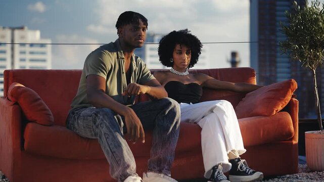 Stylish Black couple posing on red couch during photoshoot, urban fashion scene