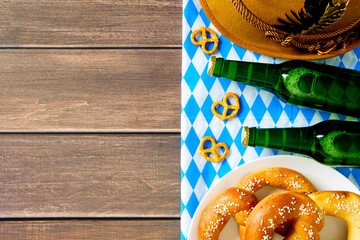 Oktoberfest flat lay with pretzels, green beer bottles, Bavarian hat, and checkered cloth on rustic...