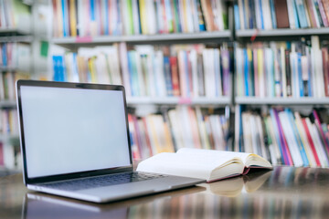 There is a laptop with a white screen and a book placed on the table in the library.
