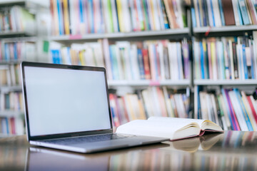 There is a laptop with a white screen and a book placed on the table in the library.
