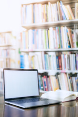 There is a laptop with a white screen and a book placed on the table in the library.
