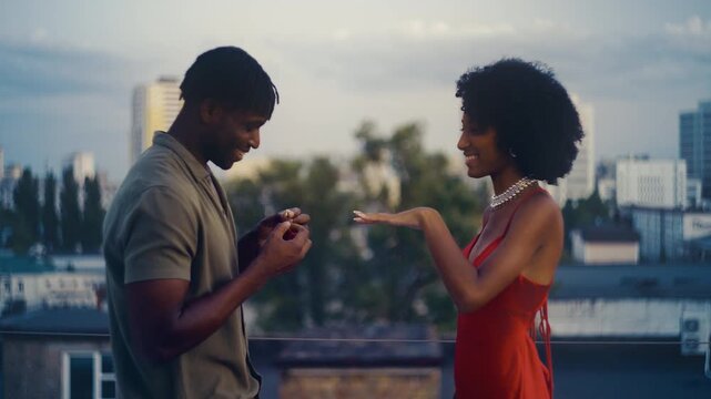 African American man proposing to girlfriend on rooftop, emotional couple moment