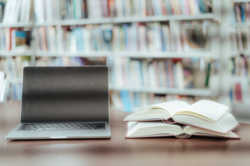 An open book with a stack of books on the table in the library beside a laptop, representing the...