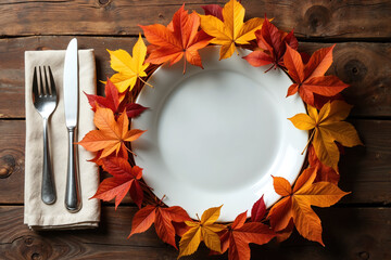 A white plate surrounded by vibrant autumn leaves, accompanied by a silver fork and knife on a beige napkin, all on a rustic wooden table.