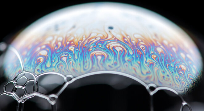 A close-up view of a soap bubble reveals a spectrum of vibrant swirling iridescent colors Smaller bubbles cluster at the bottom creating a mesmerizing abstract pattern - Powered by Adobe